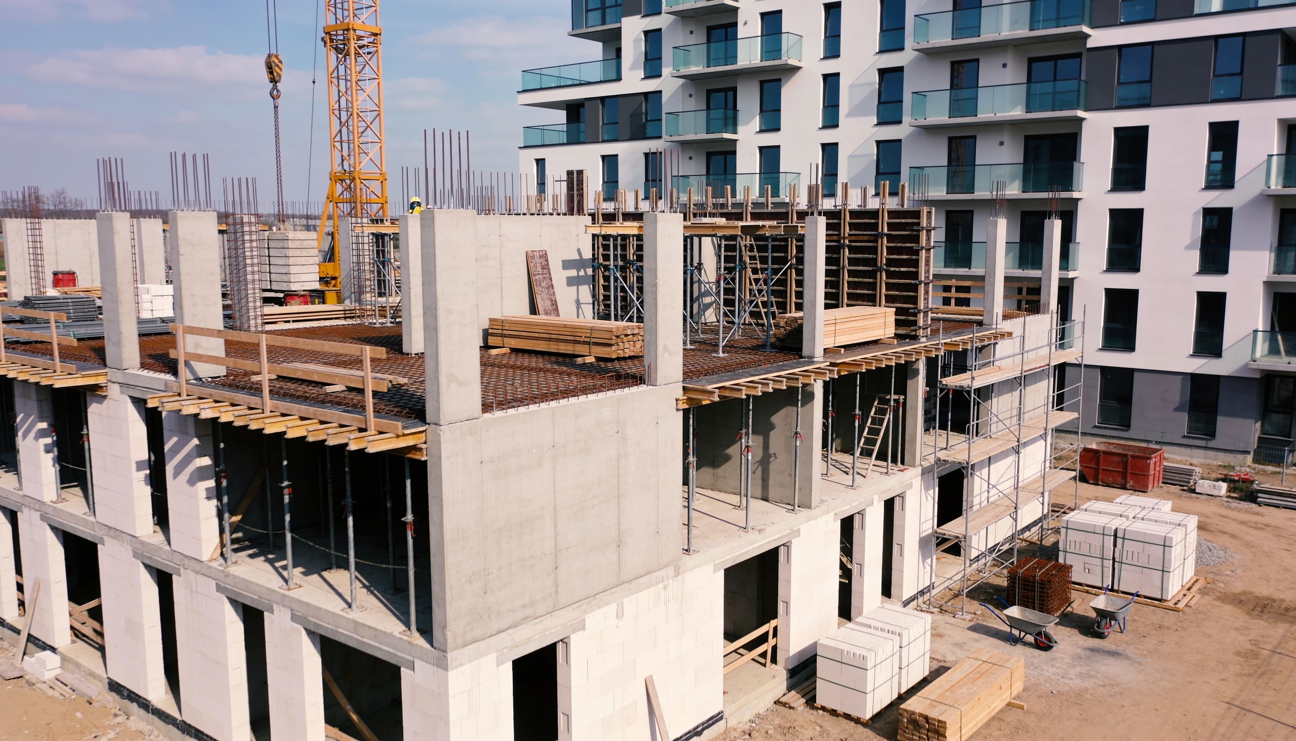Concrete structure rising behind site scaffolding and a tower crane